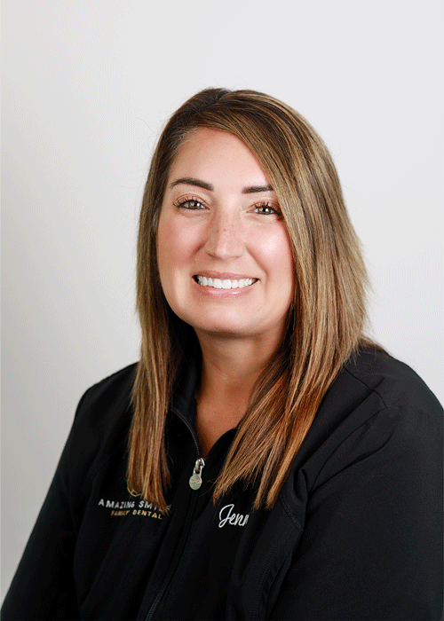 The image shows a woman smiling with a layered straight brown hair and wearing a black jacket.