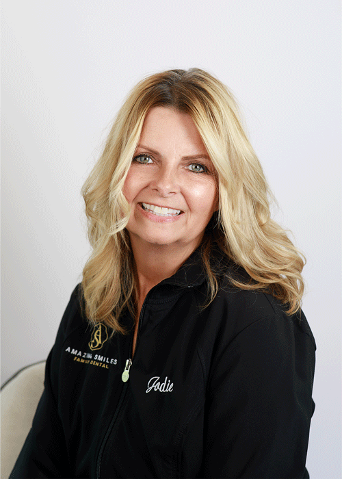The image shows a woman smiling with a long wavy blonde hair and wearing a black jacket.