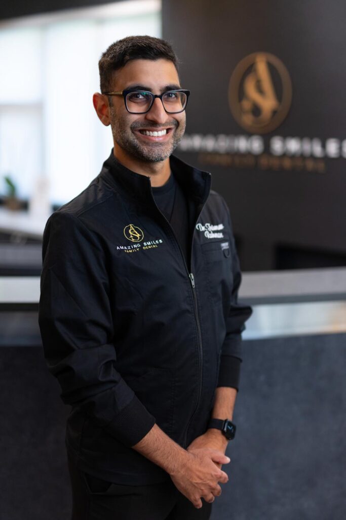 Dr. Taimoor Rahman headshot at Amazing Smiles lobby. Smiling and wearing black scrub suit