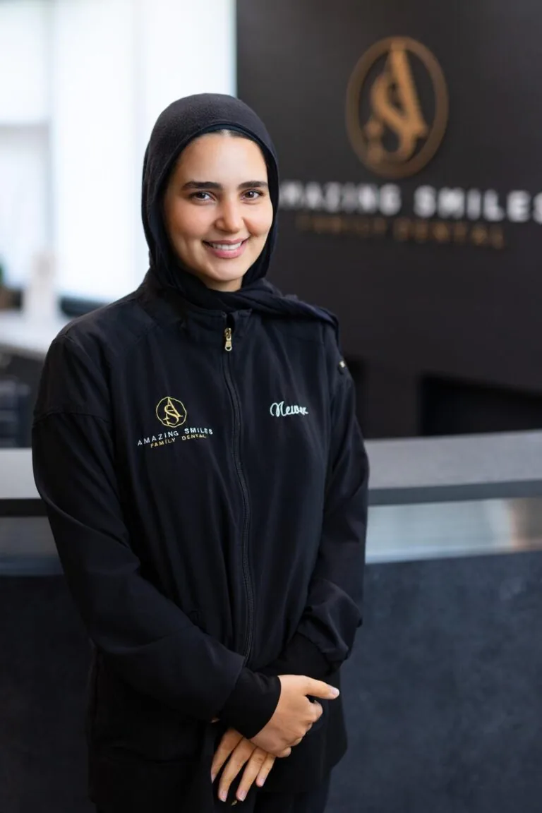 Newer Hygienist headshot at Amazing Smiles lobby. Smiling and wearing black scrub suit at Amazing Smiles lobby.